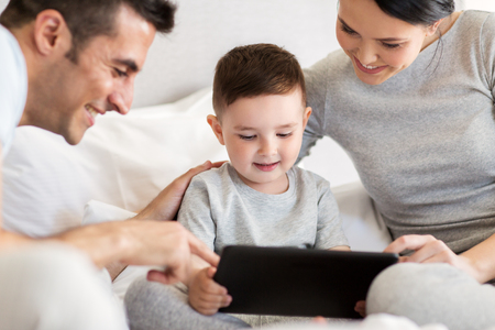 happy family with tablet pc in bed at homeの写真素材