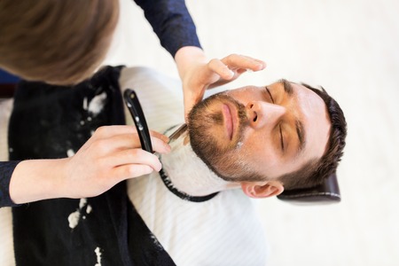 man and barber with straight razor shaving beardの写真素材