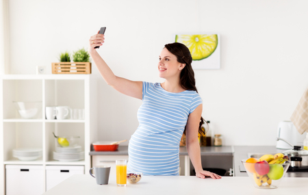 happy pregnant woman with smartphone at kitchenの写真素材