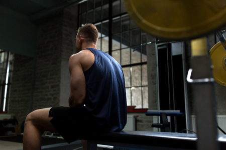 sport, bodybuilding, fitness and people concept - man sitting on weight bench in gymの写真素材