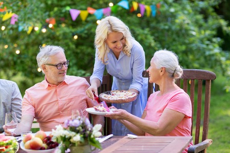 leisure, holidays and people concept - happy family sharing pie at festive dinner or summer garden partyの写真素材