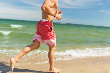 fitness, sport, people and healthy lifestyle concept - happy young man running along summer beachの写真素材