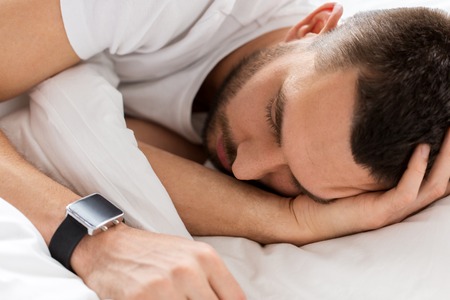 close up of man with smartwatch sleeping in bed