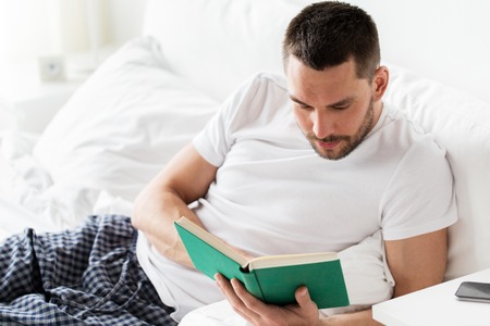 man reading book in bed at homeの写真素材
