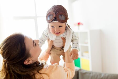 happy mother with baby wearing pilot hat at homeの写真素材