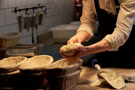 baker with dough rising in baskets at bakeryの写真素材