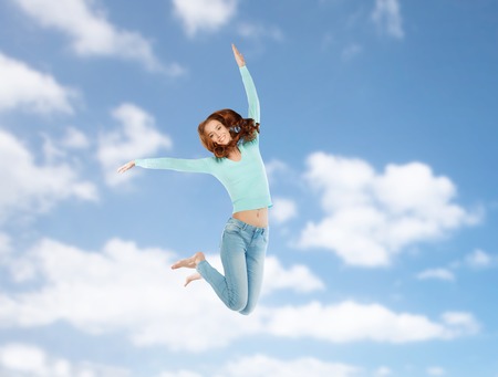 smiling young woman jumping in air over blue skyの写真素材