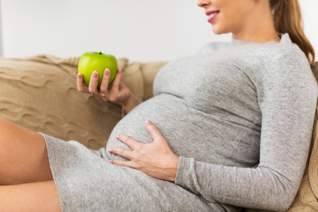 happy pregnant woman eating green apple at home