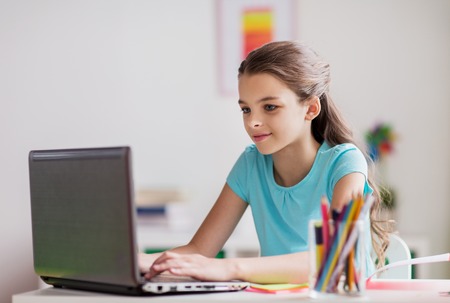 people, children and technology concept - girl typing on laptop computer at home