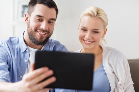 family, technology, internet and people concept - smiling happy couple with tablet pc computer at...