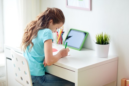 girl with tablet pc writing to notebook at homeの写真素材