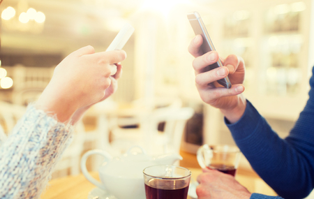 people, communication and technology concept - close up of couple with smartphones drinking tea at cafe or restaurantの写真素材