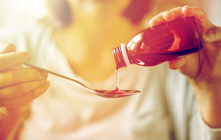 woman pouring medication from bottle to spoonの写真素材