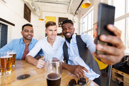 friends taking selfie and drinking beer at bar