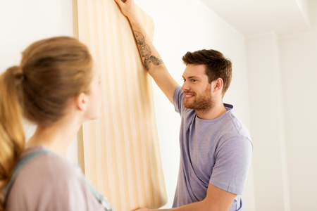 happy couple with wallpaper repairing new homeの写真素材