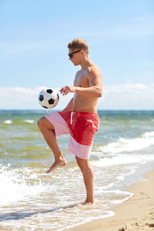 young man with ball playing soccer on beachの写真素材