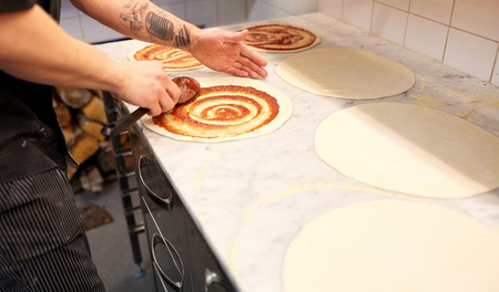 cook applying tomato sauce to pizza at pizzeriaの写真素材