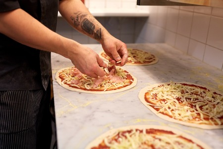 cook hands adding champignons to pizza at pizzeriaの写真素材