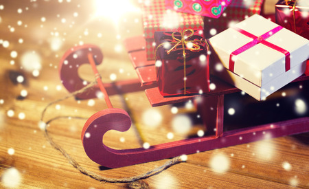 holidays, christmas, presents, new year and celebration concept - close up of many little gift boxes on red wooden sleigh on wooden tableの写真素材