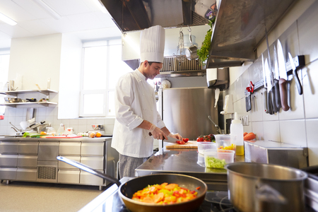 cooking food, profession and people concept - male chef cook with knife chopping tomatoes on cutting board at restaurant kitchenの写真素材