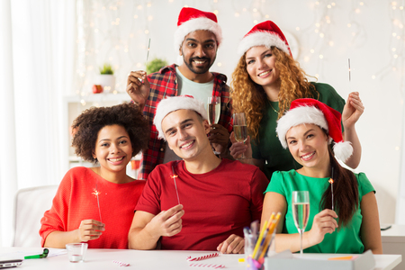 christmas, celebration and holidays concept - happy team in santa hats with sparklers and non-alcoholic sparkling wine at corporate office partyの写真素材