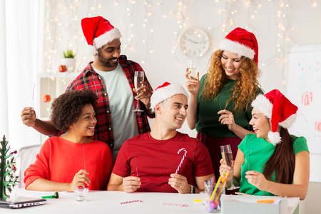 christmas, celebration and holidays concept - happy team in santa hats with sparklers and non-alcoholic sparkling wine at corporate office partyの写真素材