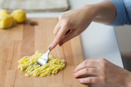 hand with fork making mashed potato on boardの写真素材