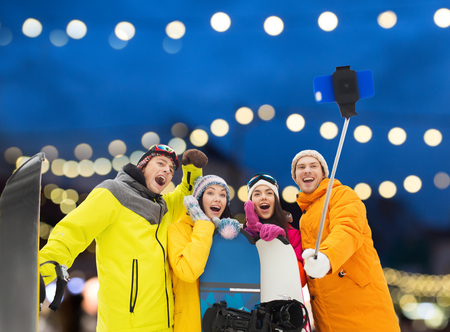 winter sport, technology and people concept - happy friends with snowboards and taking picture by...
