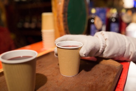 winter holidays, hot drinks and people concept - hand with cup of mulled wine at christmas market