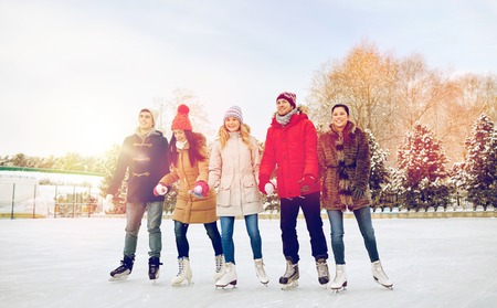 people, winter, friendship, sport and leisure concept - happy friends ice skating on rink outdoorsの写真素材