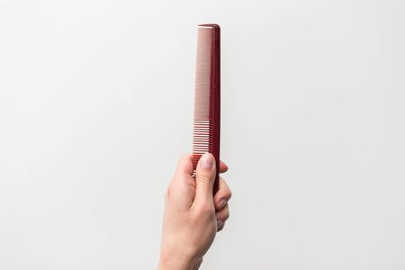 hair tools, beauty and hairdressing concept - hairdresser hand holding brown red comb on white...