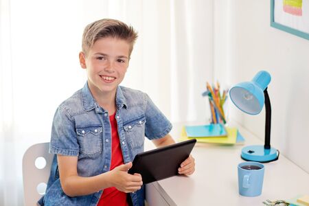 childhood, technology and people concept - smiling boy with tablet pc computer sitting at home desk