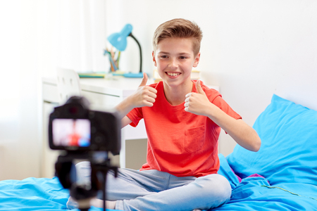 blogging, technology and people concept - happy smiling boy or blogger with camera recording video at home and showing thumbs upの写真素材
