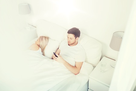 man texting message while woman is sleeping in bedの写真素材