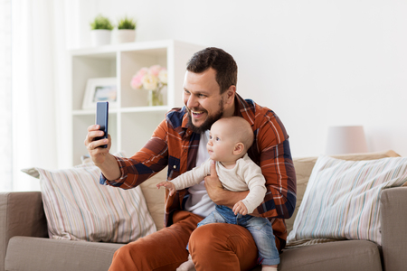 happy father with baby boy taking selfie at homeの写真素材