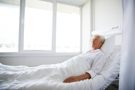 smiling senior woman lying on bed at hospital wardの写真素材