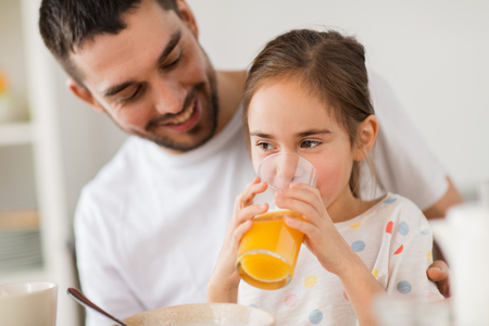 happy girl with father drinking juice at homeの写真素材