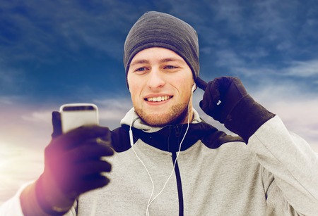 happy man with earphones and smartphone in winter