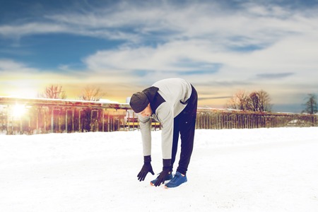 man exercising and stretching leg on winter bridge