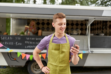 salesman in apron with smartphone at food truckの写真素材