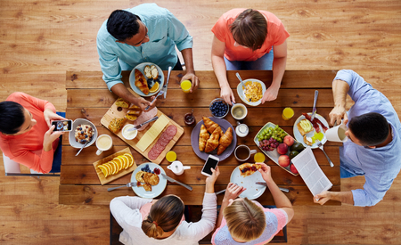 people with smartphones eating food at tableの写真素材
