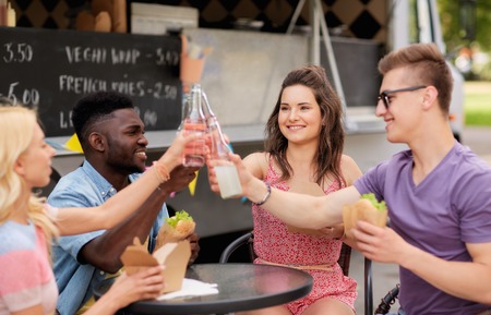 friends clinking drinks and eating at food truck
