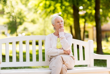 sad senior woman sitting on bench at summer parkの写真素材