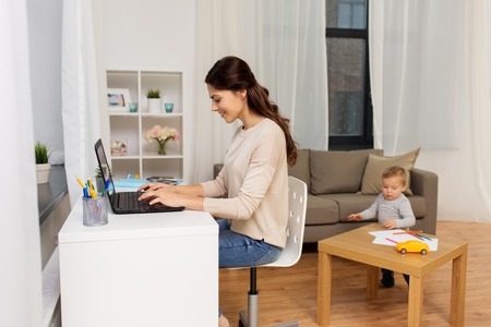 happy mother with baby and laptop working at homeの写真素材