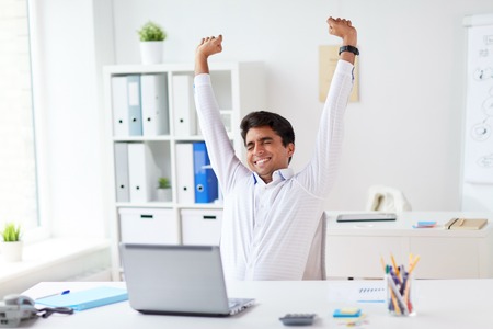 tired businessman with laptop stretching at officeの写真素材