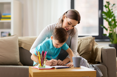 family and education concept - happy mother and little son with workbook writing or drawing at homeの写真素材