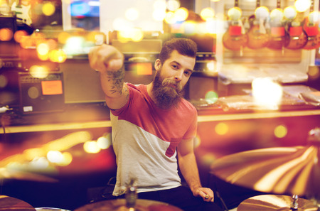 people, musical instruments and entertainment concept - male musician playing drum kit and pointing drumstick to you at music store over lightsの写真素材