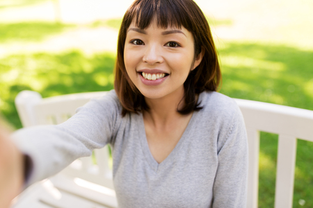 people and technology concept - happy smiling asian woman taking selfie at parkの写真素材