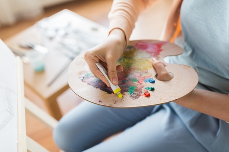 fine art, painting, creativity and people concept - close up of artist hand applying color paint to palette at studioの写真素材