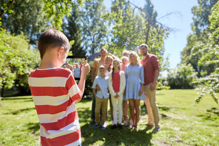 technology, generation and people concept - happy little boy taking picture of family by tablet pc computer in summer gardenの写真素材
